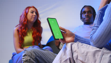 Close-Up-Of-Woman-With-Green-Screen-Mobile-Phone-Sitting-With-Gen-Z-Friends-Talking-And-Sharing-Posts-4